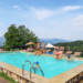Campinggasten zwemmen in zwembad Camping Pian d'Amora met uitzicht op bergen ligstoelen relaxen