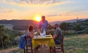 Vakantiegangers dineren buiten met uitzicht over de heuvels zonsondergang terwijl iemand wijn inschenkt op Casa & Glamping Sorriso