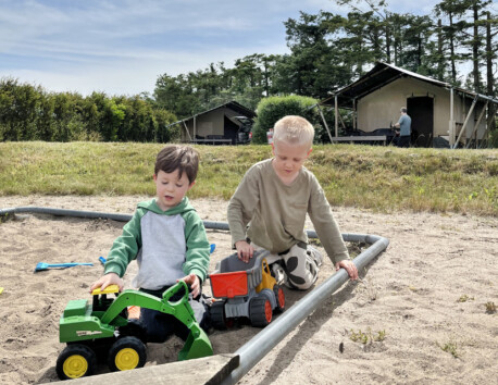 Deux enfants jouant dehors avec des véhicules jouets.