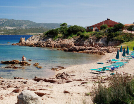 Baai strand ligstoelen parasol rotsen blauw zee Sardinië Camping Centro Vacanze Isuledda
