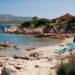Baai strand ligstoelen parasol rotsen blauw zee Sardinië Camping Centro Vacanze Isuledda