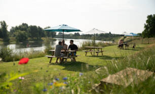Picknicktafels staan langs rivier de Maas op Camping de Boomgaard