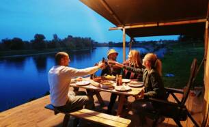 Vakantiegangers genieten van eten op veranda safaritent naast rivier de Maas Camping de Boomgaard