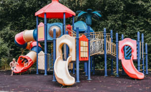 bunte Spielstruktur für Kinder. Der Spielplatz verfügt über mehrere Rutschen, Klettergeräte, eine Tunnelrutsche, eine Leiter und andere interaktive Elemente, auf denen die Kinder klettern und entdecken können.