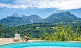 Camping Le Champ Long vrouw zit aan zwembad met op de achtergrond bergen van de Auvergne