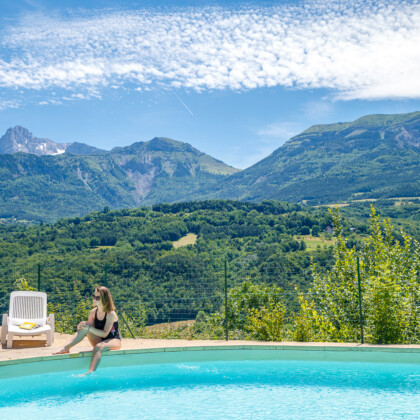 Camping Le Champ Long vrouw zit aan zwembad met op de achtergrond bergen van de Auvergne