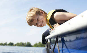 Kind met zwemvest hangt over de rand van een boot boven het water